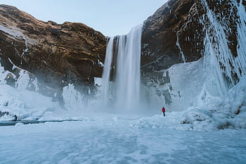 A breathtaking view of a towering waterfall amidst icy landscapes in Iceland. HD wallpaper