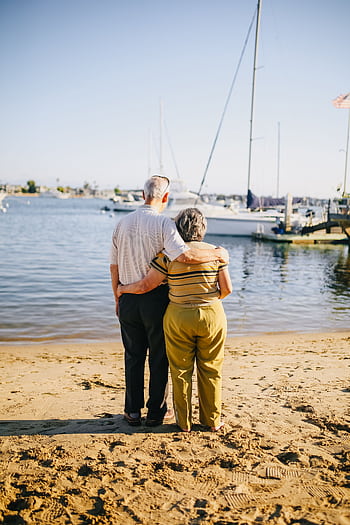 Senior couple embracing on a sunny beach. Perfect for travel and lifestyle themes. HD phone wallpaper