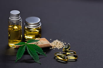 Assorted cannabis products including hemp seeds, oil, and capsules on dark background. HD wallpaper