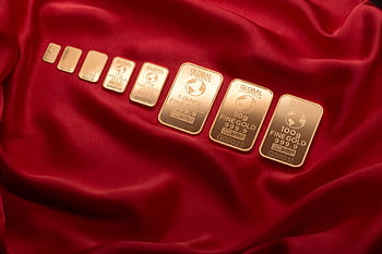 Array of fine gold bars displayed on rich red fabric, symbolizing wealth and luxury. HD wallpaper