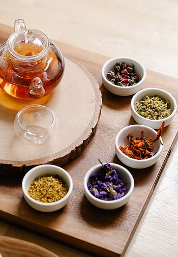 Glass teapot with herbal tea and assorted dry herbs in bowls on a wooden surface for aromatherapy. HD phone wallpaper