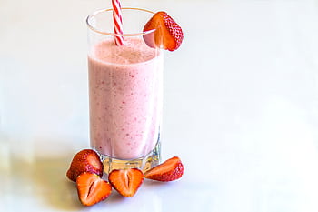 Delicious strawberry smoothie in a glass with fresh strawberries and a striped straw on a light background. HD wallpaper