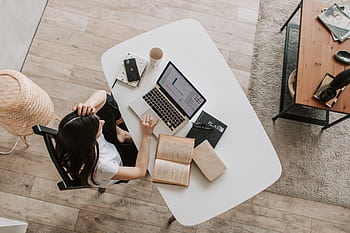 A woman multitasking with a laptop and book at a cozy home office desk. HD wallpaper