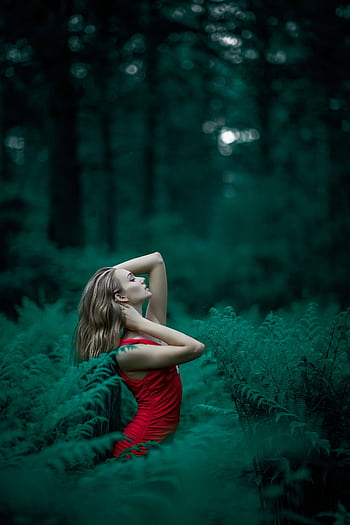 A woman poses in a vibrant red dress amidst lush green ferns in an enchanting forest setting. HD phone wallpaper