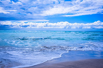 Captivating beach scene with waves and a vibrant blue sky, perfect for coastal themes. HD wallpaper
