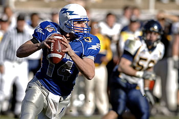 Player in blue jersey focuses on passing during a competitive football game. HD wallpaper