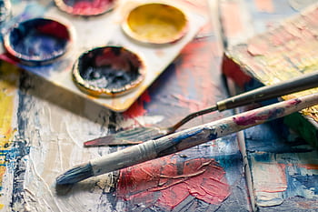 Vibrant close-up of paintbrushes and a palette on a textured canvas showcasing creativity. HD wallpaper