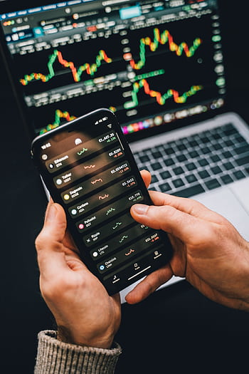 Hands holding smart with stock app, laptop displaying charts. Perfect for financial and technology themes. HD phone wallpaper