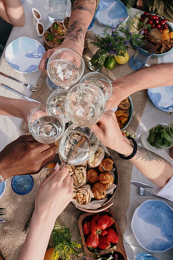A cheerful group clinks glasses during an outdoor brunch celebration, with diverse hands and appetizing food. HD phone wallpaper