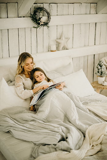 A mother and daughter enjoy a relaxing moment reading a book in a beautifully decorated bedroom. HD phone wallpaper