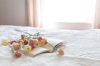 A serene bedroom scene with fresh flowers on an open book, epitomizing tranquility and elegance. HD wallpaper