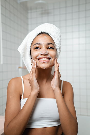 Smiling woman with face wash in a bathroom, embracing self-care and fresh skin. HD phone wallpaper