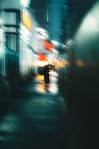 Blurry urban street scene with a solitary figure holding an umbrella under the city lights at night. HD phone wallpaper