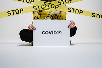 Person holding COVID-19 sign surrounded by yellow stop tape, symbolizing quarantine and safety. HD wallpaper