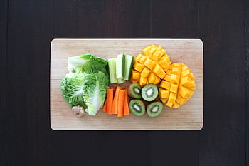 Fresh fruits and vegetables prepared for healthy salad on a wooden chopping board. HD wallpaper