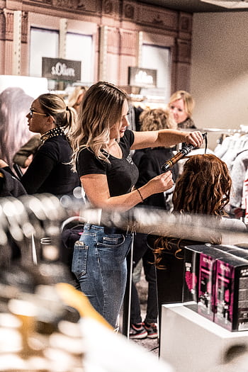 A skilled hairstylist uses a curling iron to style a client's hair in a busy salon. HD phone wallpaper