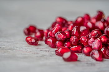 Vivid close-up of juicy red pomegranate seeds scattered on a surface. HD wallpaper