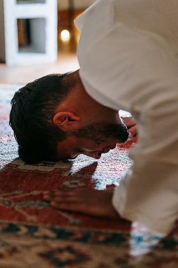 A person in traditional attire bows in prayer on a patterned rug within a room. HD phone wallpaper