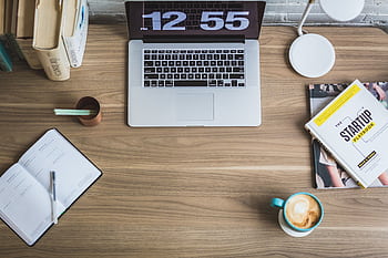 Flat lay of a modern workspace with a laptop, coffee cup, and startup books on a wooden desk. HD wallpaper