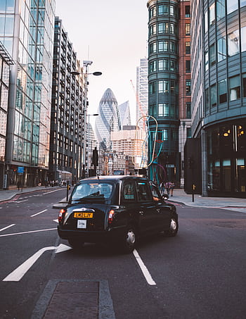 Classic black taxi navigating the streets of London with iconic skyscrapers in the background. HD phone wallpaper