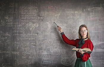 A confident woman lecturer explains concepts on a chalkboard in a classroom. HD wallpaper