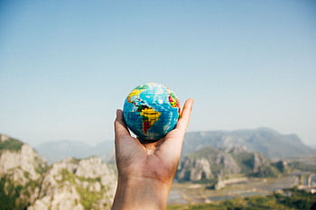 Hand holding a globe against a mountain background symbolizing travel and exploration. HD wallpaper