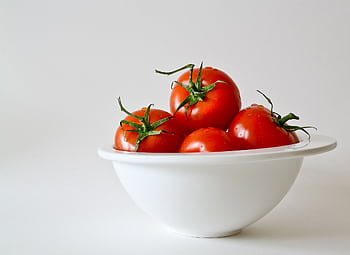 Vibrant red tomatoes in a white bowl, emphasizing freshness and simplicity. HD wallpaper