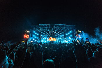 Vibrant crowd enjoying an epic concert under bright stage lights with smoke effects. HD wallpaper