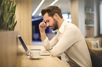 A thoughtful man in a shirt works on his laptop at a modern indoor office space. HD wallpaper