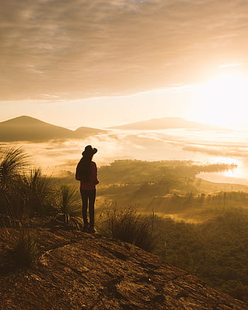 Silhouette of a person hiking and enjoying a sprawling landscape during a golden sunrise on a misty morning. HD phone wallpaper