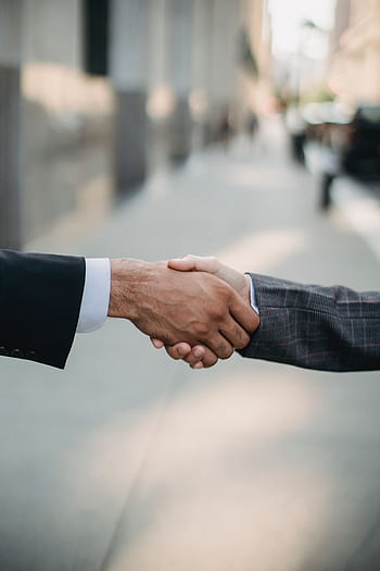 Two businessmen shaking hands outside, symbolizing cooperation and agreement in a city setting. HD phone wallpaper