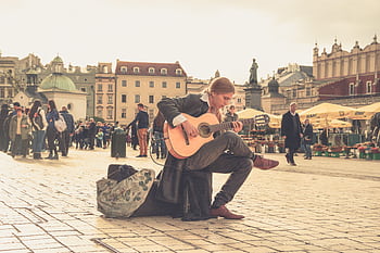A street performer playing guitar in a vibrant old town square with a lively crowd. HD wallpaper