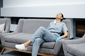 Nurse in scrubs takes a break, resting on a comfy hospital couch after a long shift. HD wallpaper