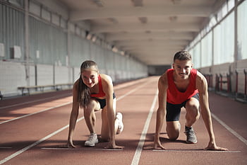 Two athletes, a man and a woman, ready to sprint on an indoor track, embodying fitness and determination. HD wallpaper