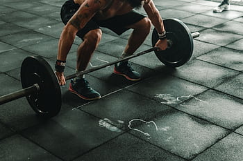 A muscular man in a gym preparing to lift a heavy barbell, showcasing strength and fitness. HD wallpaper