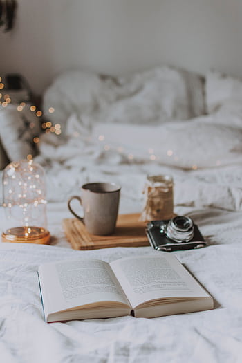 A cozy bedroom scene with coffee, books, and warm lighting, perfect for relaxation. HD phone wallpaper