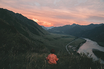 Woman sitting above a river-lined valley at dusk, sky, road, nature, mountains, woman, river, dusk, green, valley, clouds, sunset HD wallpaper