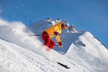 Dynamic capture of a skier racing downhill in snowy mountains, showcasing adrenaline and winter sport excitement. HD wallpaper