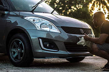 A man carefully cleans a car hood at sunset, focusing on details. HD wallpaper