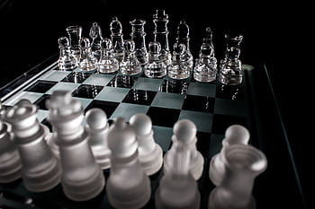 Close-up of frosted and clear glass chess pieces on a chessboard, symbolizing strategy and intelligence. HD wallpaper