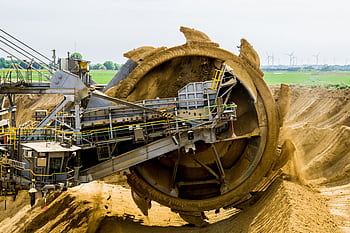 A large bucket wheel excavator working in an open pit mine against a green landscape. HD wallpaper