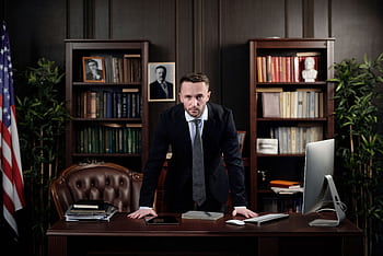 Confident businessman standing at desk with USA flag in office library. HD wallpaper