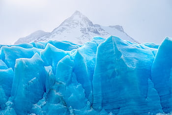A stunning view of a vibrant blue glacier set against snow-capped mountains, showcasing winter's beauty. HD wallpaper