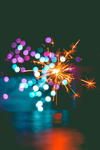 A dynamic sparkler igniting against a colorful bokeh background, perfect for celebrations. HD phone wallpaper