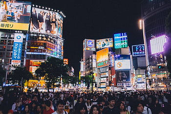 A bustling crowd at Shibuya Crossing under the bright lights of Tokyo's urban night scene. HD wallpaper