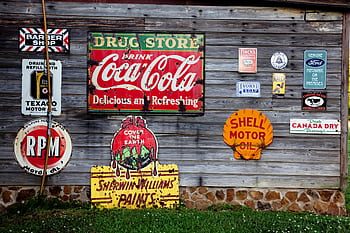Collection of vintage advertising signs on rustic wooden wall showcasing classic brands. HD wallpaper