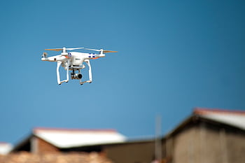 Aerial drone with camera hovering over rooftops beneath a clear blue sky, showcasing modern technology in action. HD wallpaper