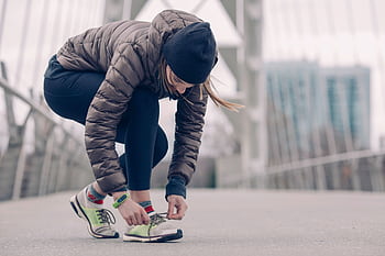 Woman in activewear tying running shoes on a city bridge, ready for a winter jog. HD wallpaper