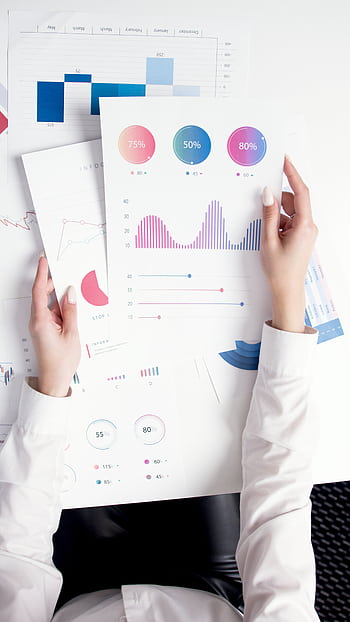 Close-up of hands analyzing colorful business data reports in an office setting. HD phone wallpaper