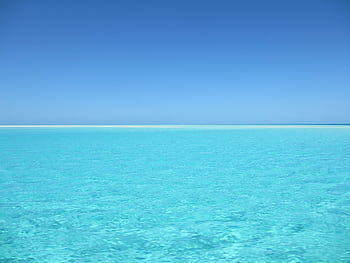 A serene blue ocean with crystal clear water under a vivid blue sky, perfect for relaxation. HD wallpaper